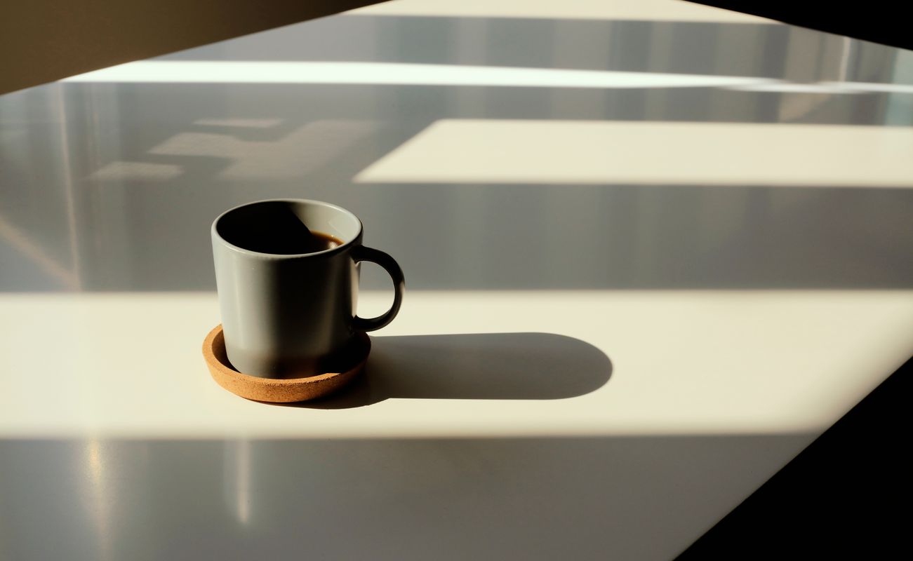 Eine Tasse Kaffee auf einem weißen Tisch, umgeben von Schatten und Lichtmustern.
